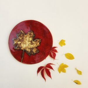 Ceramiczny czerwony talerz z motywem liścia klonu. Jesienne liście.